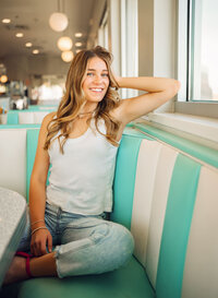 Senior portrait at Sunliner Diner in Gulf Shores, Alabama — sitting in a booth, laughing with her
hand in her hair.