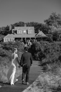 Bride and Groom walk down board walk towards ceremony.
