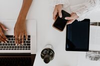 An overhead shot of a desk with hands working on a laptop and on an iPhone | Venue Business Boot Camp