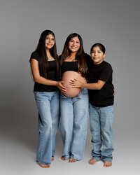 Pregnant mom standing with her children, all smiling and holding her baby bump during a family maternity photoshoot in the Inland Empire by Kaitlyn Dawn Photography.