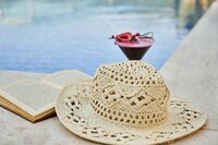 a straw hat, book, and martini glass w red liquid sit poolside