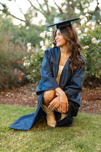 High school graduate sitting on grass wearing a cap and gown, outdoor senior portrait by Kaitlyn Dawn Photography.