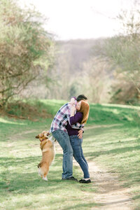 couple hugging in field with corgi