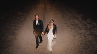 Bride and groom walking down dirt road at night.
