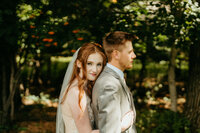 Bride embraces groom from behind during romantic outdoor forest wedding photoshoot.