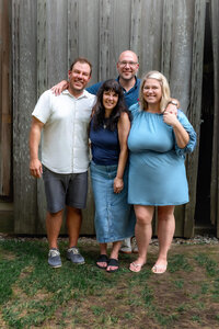 Mother standing with her three adult children in front of rustic wooden barn during extended family session in New Bern North Carolina