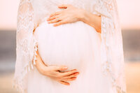 A close up picture of a mother's hands wrapped around her baby bump.