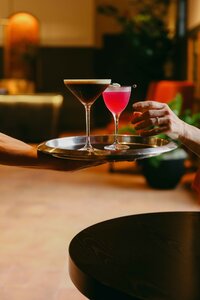 Server delivering two cocktails on a brass tray in the Lobby Bar