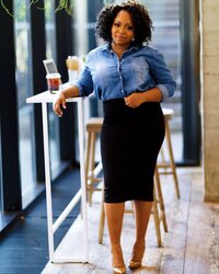 african american woman with natural hair in a blue button up leaning on a dining table