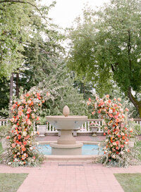 a summer flower arch made of orange roses in front of lsirmont manors fountain.