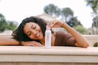 Model resting on a stone balustrade beside the Evian facial spray, warm daylight