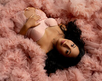 Expecting mother lying in a soft pink tulle maternity gown with hands on her belly during a studio maternity photoshoot by Kaitlyn Dawn Photography.