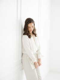 Local Dallas business owner leaning against the wall in a Dallas photography studio as she holds books and loos down.