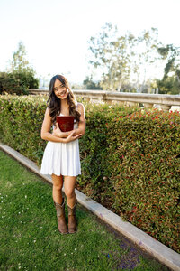 High school senior girl in a white dress and cowboy boots standing in a garden path, outdoor senior portrait by Kaitlyn Dawn Photography.