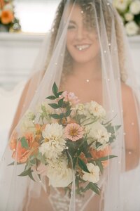 Bride behind pearl veil holding peach and ivory textured bouquet by Flowergirl Cville, Charlottesville florist, at Virginia Creative Collective | Photo by Lyn Waldrop Photography