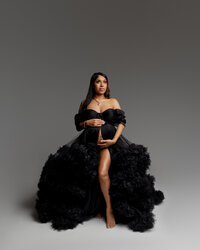 Pregnant woman seated in a black tulle maternity gown during a studio maternity portrait session by Kaitlyn Dawn Photograph