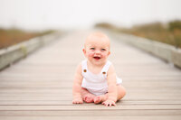 Charleston Baby Milestone Photographer - Baby laughs on a board walk by the beach in Isle of Palms during his Baby Milestone Portrait Session in Charleston.
