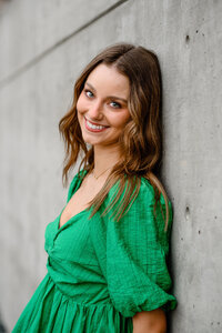 A Littleton senior photographer captures a Denver senior girl wearing a green dress leaning up against a concrete wall.
