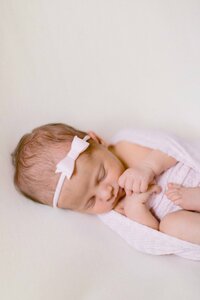 newborn baby girl snuggled in a pink swaddle with a pink bow on her head