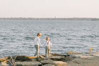 Two young brothers playing on the rocks by a lake.