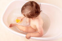 top view of toddler in white tub holding yellow duck during milestone session