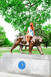 Senior wearing white and blue floral dress sitting on tiger at TSU