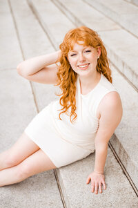 Senior girl sitting on stairs smiling at camera while she plays with her hair