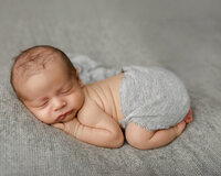 Peacefully sleeping newborn baby posed on a neutral gray blanket wearing a soft gray wrap during a natural studio newborn photography session captured by Kaitlyn Dawn Photography.