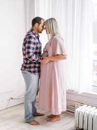 Pregnant mom and her husband are embracing, their foreheads touching and their hands are on mom's belly