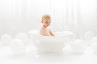 Baby plays in a splash bath during his first birthday Cake Smash Photoshoot at Holy City Babies Portrait Studio in Charleston, SC.