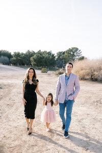 The Parker family walking hand in hand along a sunlit desert path in Las Vegas, featuring parents and young daughter in coordinated outfits during a natural light family portrait session.