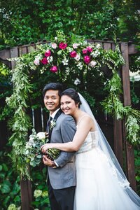Floral ceremony arbor of greenery, magenta and white roses with bride and groom