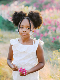 A little girl looking at the camera surrounded by sweet pea flowers