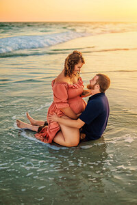 Pregnant couple sitting in the surf during golden hour maternity photos on the North Carolina coast