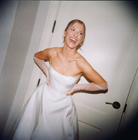 Candid film photo of bride Callie laughing with hands on her hips, wearing a strapless wedding gown and sheer gloves, taken at Burritt on the Mountain during her wedding.