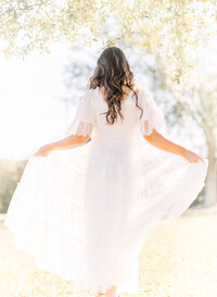 Brunette woman twirls white dress and sheer fabric glows in the sun.