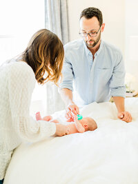 Parents smiling and interacting with their newborn on a bed during a relaxed lifestyle newborn photography session at home.