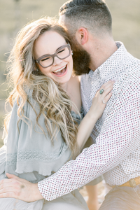 A light filled photo in a local Dallas/Fort Worth park of parents smiling and embracing each other for their family portraits together.
