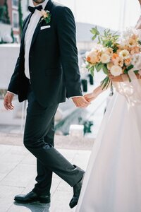 bride-groom-with-bouquet-walk-holding-hands-along-sea-cropped-faceless