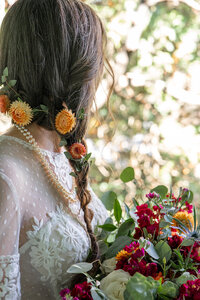 A bride with braided hair with flowers in her hair holding a bouqet