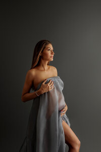portrait of pregnant woman wrapped in flowing fabric during fine art maternity portrait session in North Hollywood, dark moody setting