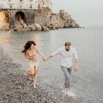 Engaged couple running barefoot along the beach on the Amalfi Coast, captured by a destination wedding photographer.