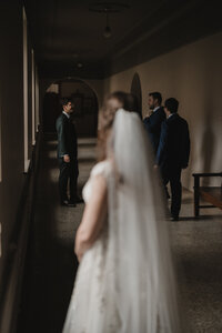 Mariée floue au premier plan sous son voile, marié et garçons d'honneur discrets dans un corridor voûté, moment de first look à l'Auberge Willow Inn, Hudson