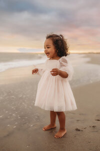Charleston Baby Milestone Photographer - Toddler delights at the water on the beach during her Baby Milestone Portrait Session in Charleston, SC.