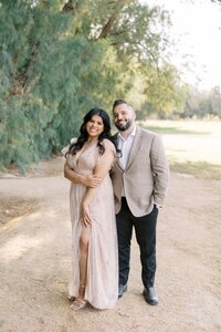 Portrait of the Dilorio family parents standing together and smiling during a natural outdoor photography session in Las Vegas, surrounded by soft greenery and warm light.