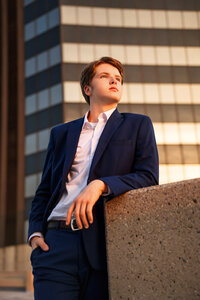 Senior portrait in downtown Mobile, Alabama— wearing a blue suit looking off into the golden sunset with an office building in the background.