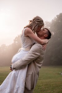 groom lifts bride up for kiss at sunset