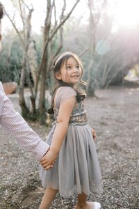 Candid portrait of the Dilorio family’s daughter holding hands and smiling in soft golden light during an outdoor photography session in Las Vegas.