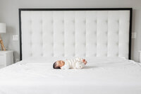 Newborn baby boy stretching on big bed