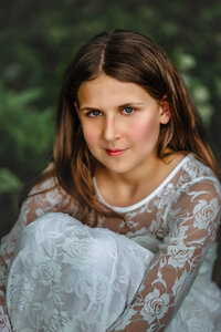 Close up portrait of young girl in white lace dress with soft natural light and green background